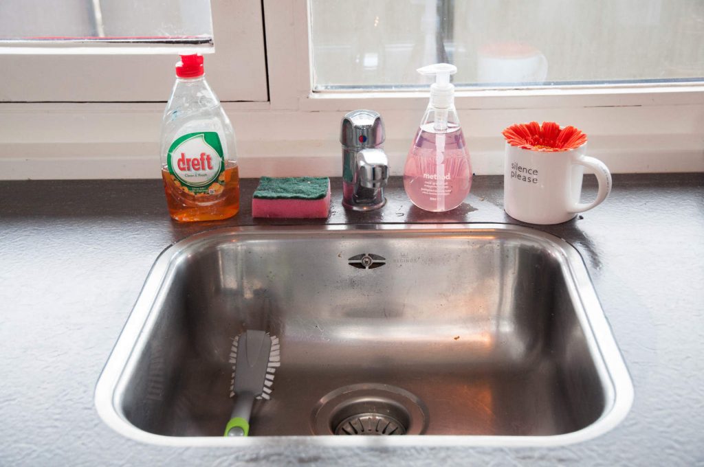A photo of a sink surrounded by cleaning supplies. First Kitchen Essentials for Your New Apartment