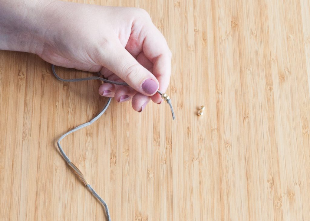 3 Easy DIY Bracelets You'll Actually Want to Wear. Image Description: A hand beading gold tubes onto a cord.